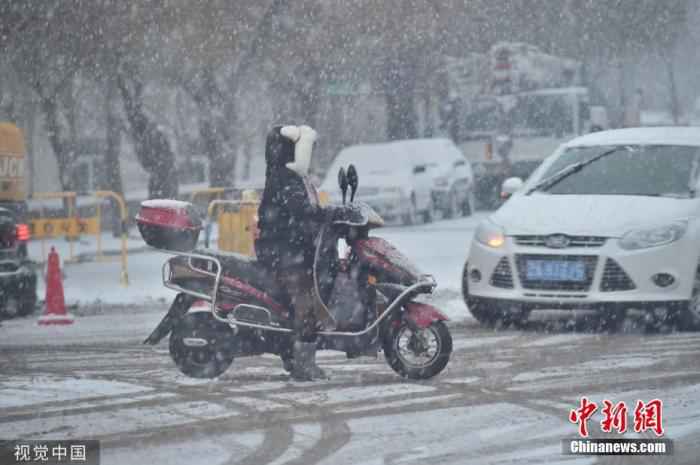 市民骑着电动车在雪中出行。图片来源：视觉中国